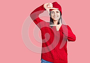 Young beautiful girl wearing sweater and wool cap smiling making frame with hands and fingers with happy face