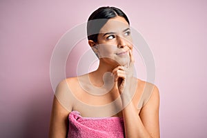 Young beautiful girl wearing towel shower after bath standing over isolated pink background with hand on chin thinking about