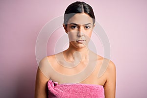 Young beautiful girl wearing towel shower after bath standing over isolated pink background with serious expression on face