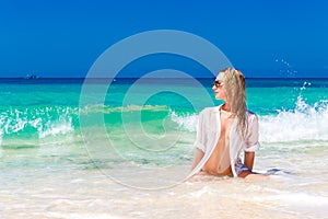 Young beautiful girl in wet white shirt on the beach. Blue trop