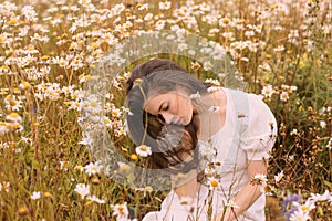 Young beautiful girl in white dress sitting in chamomile field