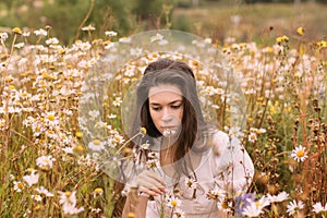 Young beautiful girl in white dress smelling flowers in chamomile field
