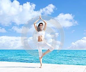 Young and beautiful girl in white sportswear doing yoga on a woo