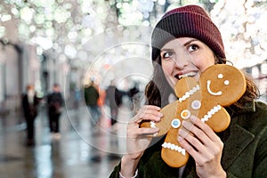 Young beautiful girl, woman is biting huge funny gingerbread man.Christmas shopping.Walking on market street in big city decorated