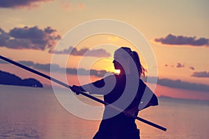 Young beautiful girl woman blond doing kung fu with bamboo stick on the seashore at sunset, fight