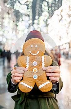 Young beautiful girl, woman with huge funny gingerbread man. Christmas shopping. Walking on market street in big city decorated