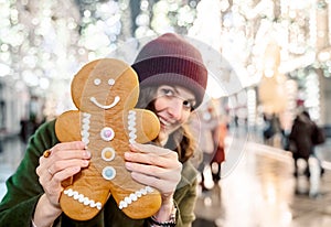 Young beautiful girl, woman with huge funny gingerbread man. Christmas shopping. Walking on market street in big city decorated