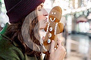 Young beautiful girl,woman is kissing huge funny gingerbread man.Christmas shopping.Walking on market street in big city decorated