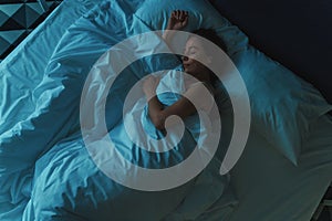 Young beautiful girl or woman sleeping alone in big bed at night, top view, blue toned