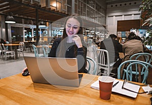 Young, beautiful girl working with laptop and drinking coffee at a wooden table