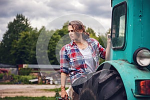 Young beautiful girl is working on a tractor in a field on a far