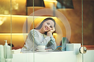 Young beautiful girl works in a cafe with a laptop, looks away dreaming and making plans