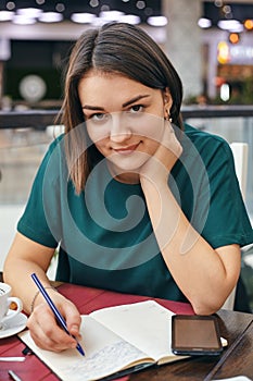 Young beautiful girl writes something in her notebook while sitting in the office