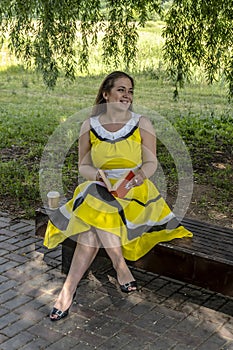 Young beautiful girl in a yellow dress with a book in the park. Reads, studies, rest