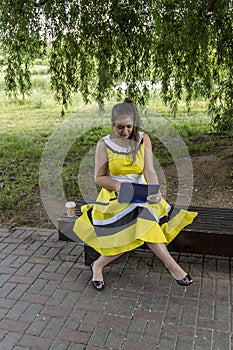 Young beautiful girl in a yellow dress with a laptop in the park. Works, learns, communicates online, making online shopping,