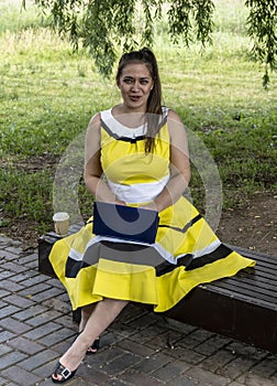 Young beautiful girl in a yellow dress with a laptop in the park. Works, learns, communicates online, making online shopping,