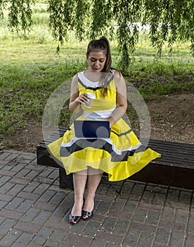 Young beautiful girl in a yellow dress with a laptop in the park. Works, learns, communicates online, making online shopping,