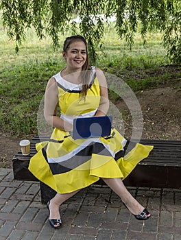 Young beautiful girl in a yellow dress with a laptop in the park. Works, learns, communicates online, making online shopping,