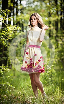 Young beautiful girl in a yellow dress in the woods. Portrait of romantic woman in fairy forest. Stunning fashionable teenager