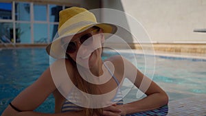 a young beautiful girl in a yellow hat and sunglasses is relaxing in the pool and smiling. Vacation, rest at the hotel