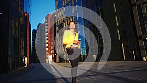 Young beautiful girl in a yellow jacket staying near office with the phone. Business woman using smartphone at the