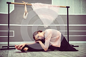 young beautiful graceful ballerina resting in ballet class sitting on the floor, ballet shoes, a pink skirt and ballet barre in t
