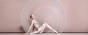 Young beautiful graceful caucasian ballerina practice ballet positions in tutu skirt. Classical Ballet dancer sitting on the floor