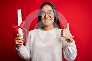 Young beautiful graduate asian woman holding university degree diploma over red background happy with big smile doing ok sign,