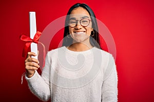 Young beautiful graduate asian woman holding university degree diploma over red background with a happy face standing and smiling