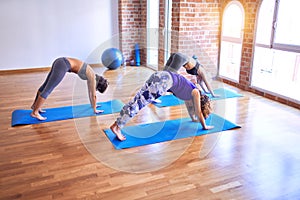 Young beautiful group of sportswomen practicing yoga doing downward-facing dog pose at gym
