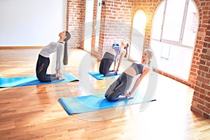 Young beautiful group of sportswomen smiling happy practicing yoga doing camel pose at gym