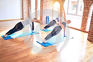 Young beautiful group of sportswomen smiling happy practicing yoga doing side plank pose at gym