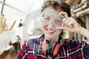 Young beautiful handy professional happy female strong carpenter portrait wearing protective goggles working in