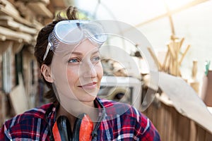 Young beautiful handy professional happy female strong carpenter portrait wearing protective goggles working in