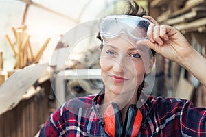 Young beautiful handy professional happy female strong carpenter portrait wearing protective goggles working in