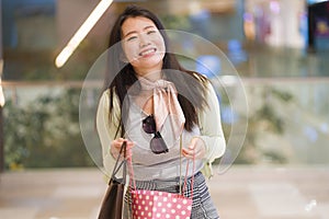 Young beautiful and happy Asian buying at shopping mall - young attractive and stylish Japanese woman holding shopping bags at