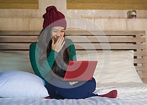 Young beautiful happy Asian Chinese girl in winter beamy relaxed on bed using laptop computer having fun enjoying online movie or