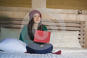 Young beautiful happy Asian Chinese girl in winter beamy relaxed on bed using laptop computer thoughtful and pensive enjoying soci