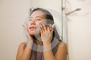Young beautiful and happy Asian Chinese woman applying serum facial skin care and face treatment in the bathroom enjoying morning photo