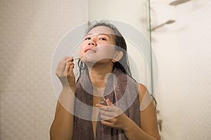 Young beautiful and happy Asian Chinese woman applying serum facial skin care and face treatment in the bathroom enjoying morning photo