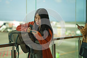 Young beautiful and happy Asian Chinese woman checking mobile phone holding passport at airport departure lounge carrying backpack