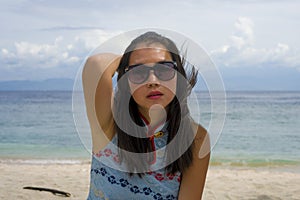 Young beautiful and happy Asian Chinese woman in chic Summer dress and sunglasses posing relaxed as tourist at tropical beach