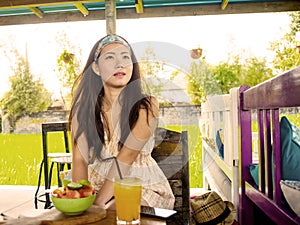 Young beautiful and happy Asian Chinese woman drinking orange juice eating healthy salad at organic food coffee shop outdoors enjo