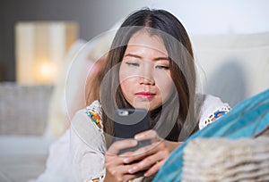 Young beautiful and happy Asian Chinese woman on her 20s or 30s lying at living room sofa couch using internet mobile phone lookin