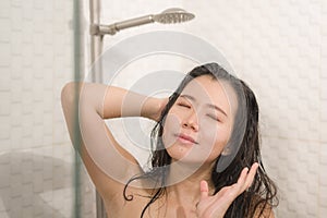 Young beautiful and happy Asian Chinese woman taking a shower in the bathroom washing her hair enjoying morning hygiene in