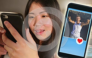 Young beautiful and happy Asian Chinese woman using internet online dating app on mobile phone sending like message to handsome Ca