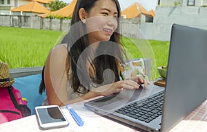 Young beautiful and happy Asian Chinese woman working outdoors with laptop computer networking green grass background cafe as digi