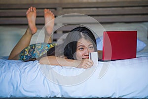 Young beautiful happy Asian Japanese girl using credit card internet banking on laptop computer at home in bed shopping online e-c