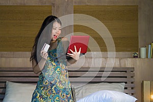 Young beautiful happy Asian Japanese woman using credit card internet banking on laptop computer at home in bed shopping online e-