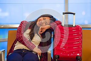 Young beautiful and happy Asian Korean tourist woman with travel suitcase in airport sitting at departures lounge gate waiting for